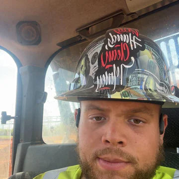 Man in a hi-vis vest wearing a Dirty Hands Clean Money hydro dipped hard hat in a truck cab